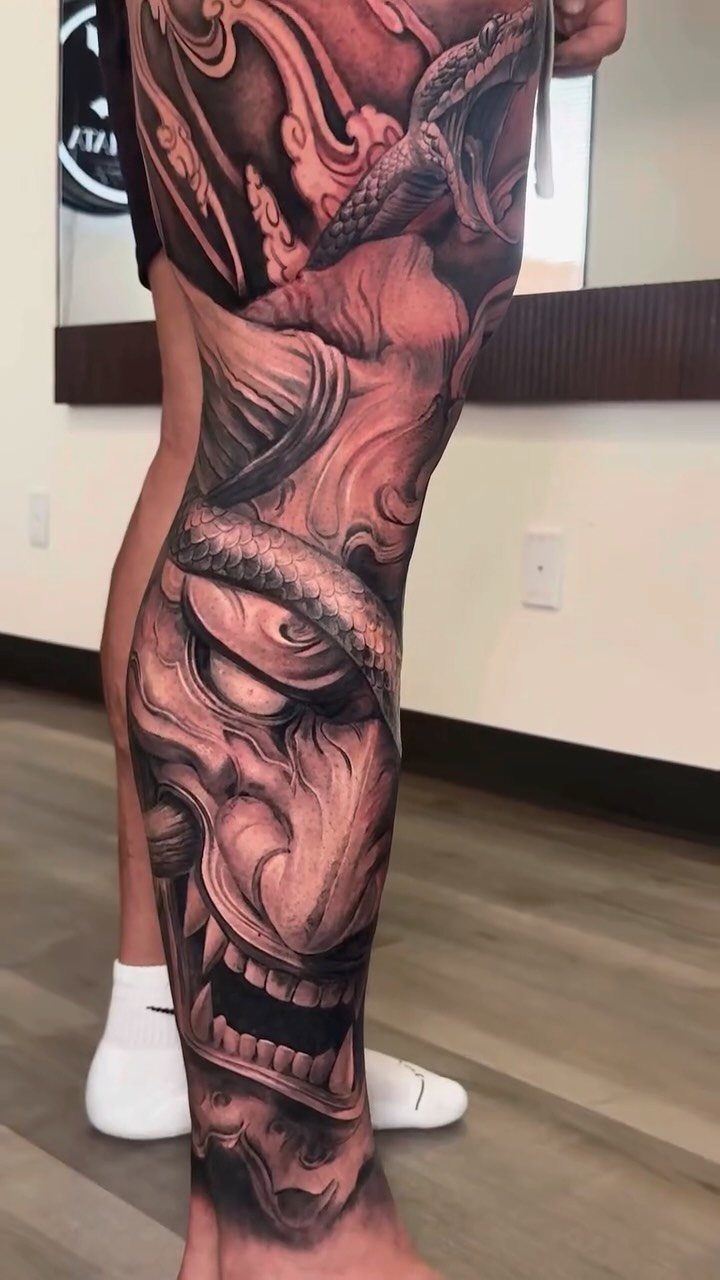 Full leg tattoo featuring a Japanese demon face, dragon, and swirling waves.