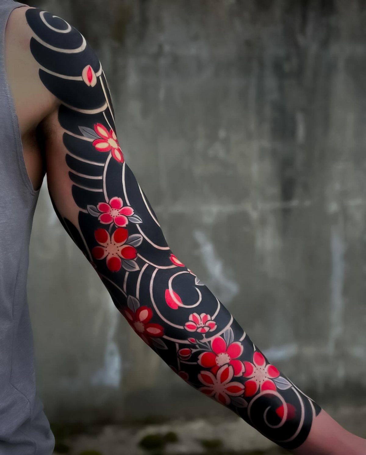 Arm with a full sleeve tattoo of red flowers and black swirling waves.