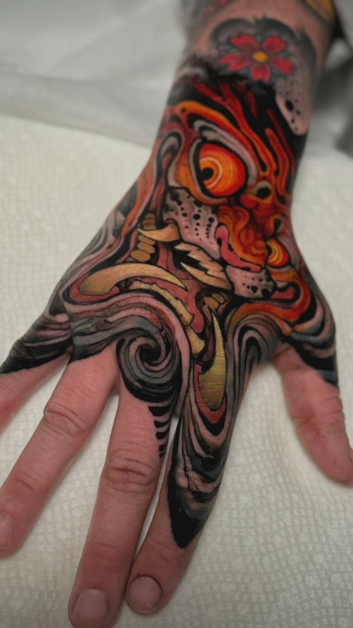 Colorful Japanese tattoo of a demonic face and waves on a person's hand.