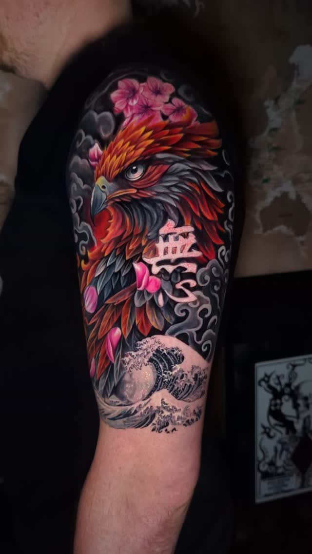 Phoenix tattoo on an arm with cherry blossoms, clouds, and ocean waves.