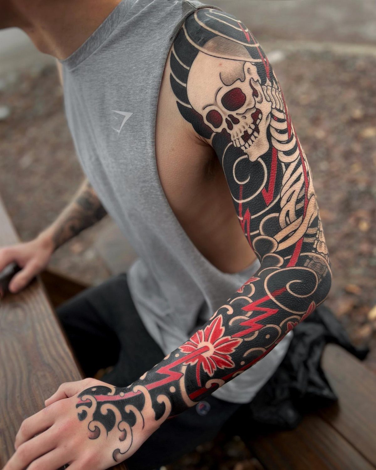 Full arm Japanese tattoo sleeve featuring a skull and red floral patterns.