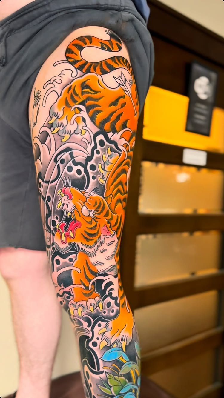 Orange tiger Japanese tattoo on a leg with grey swirling waves and clouds.