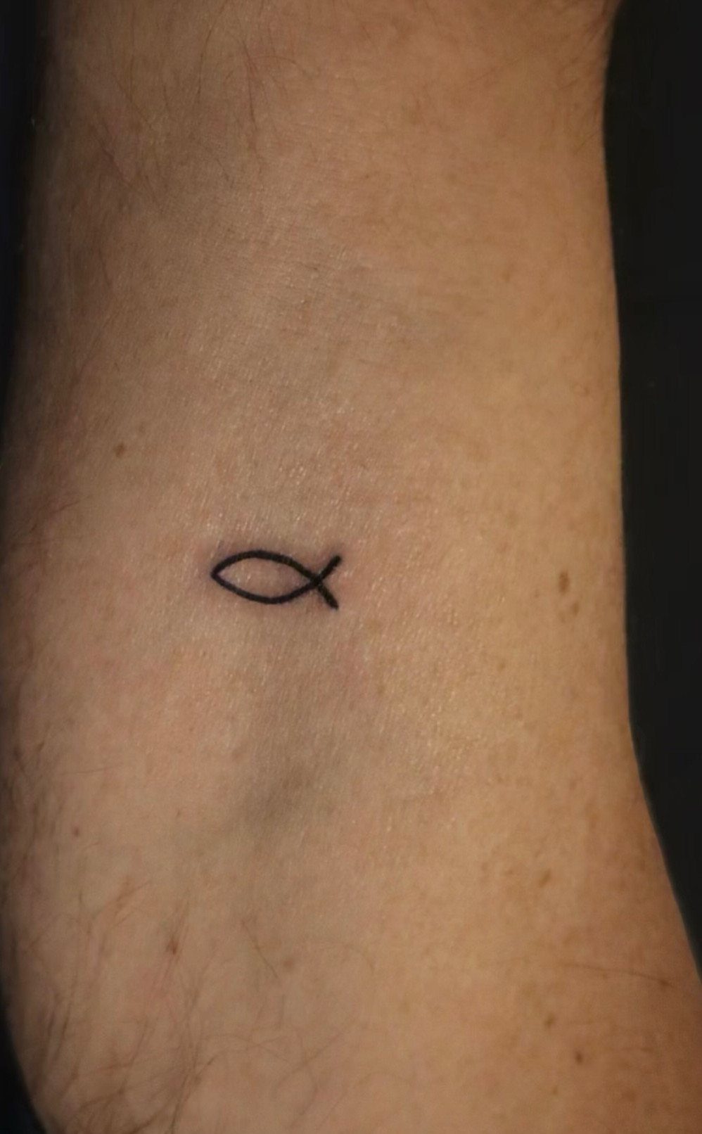 Small black ink fish symbol tattoo on the inner wrist of a person