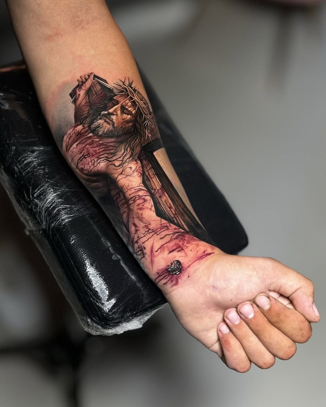 Forearm tattoo of Jesus wearing a crown of thorns and carrying a wooden cross.