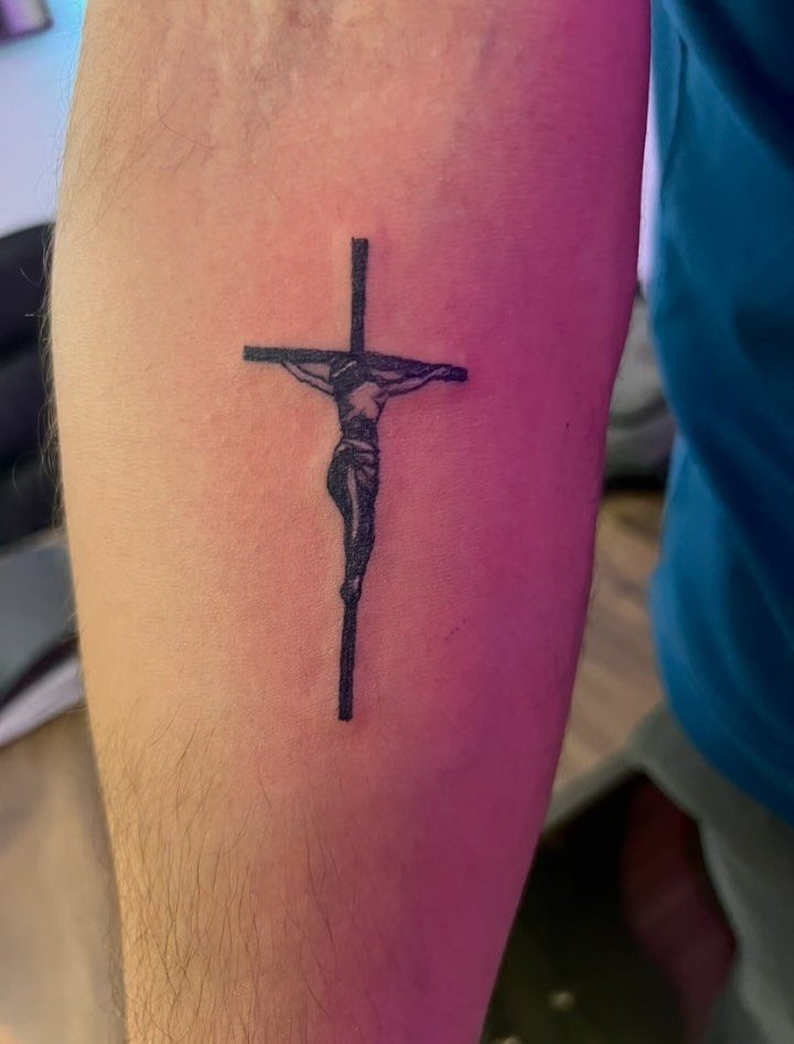Jesus on the cross tattoo in black ink on a person's forearm