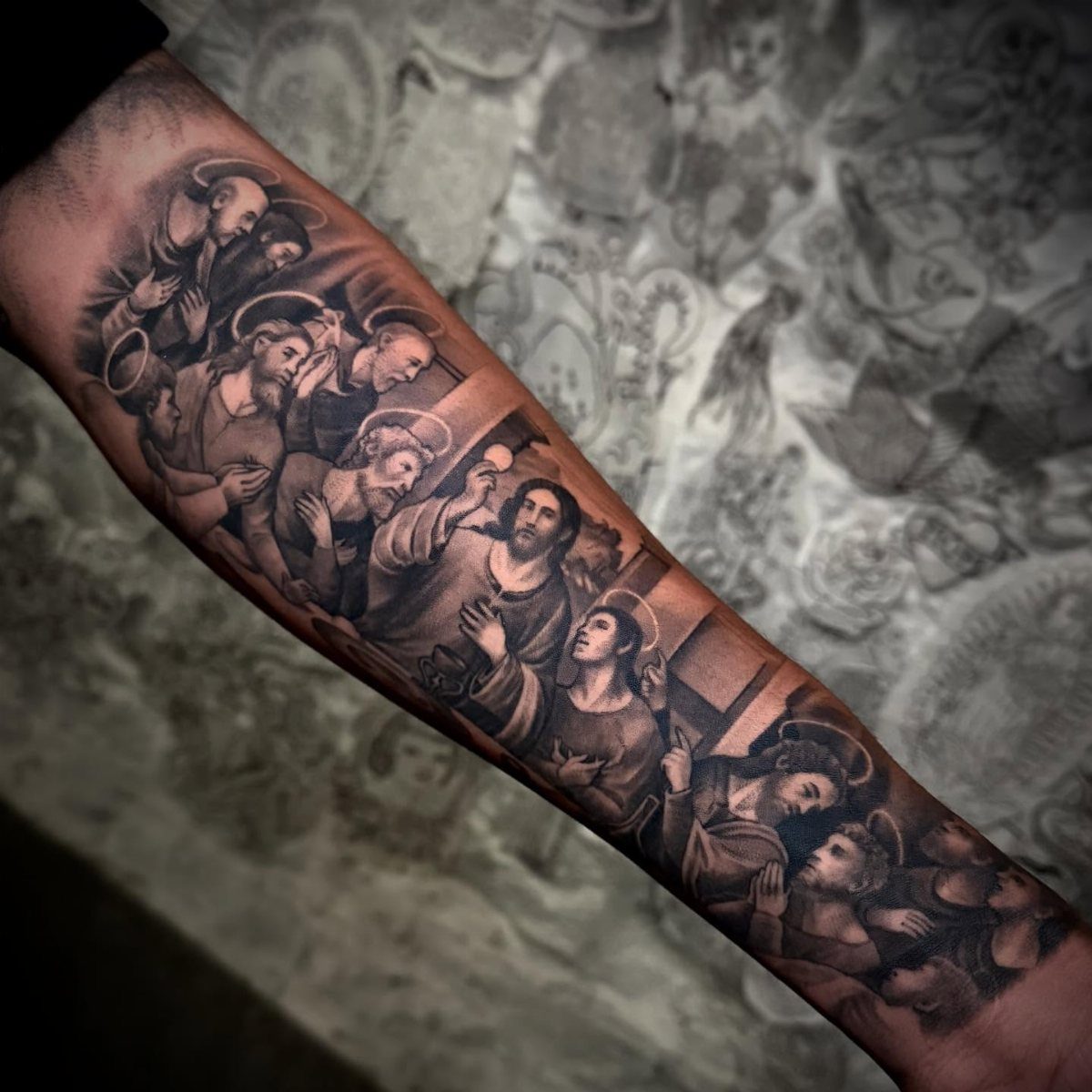 Last Supper tattoo on a forearm showing Jesus and disciples in black and grey