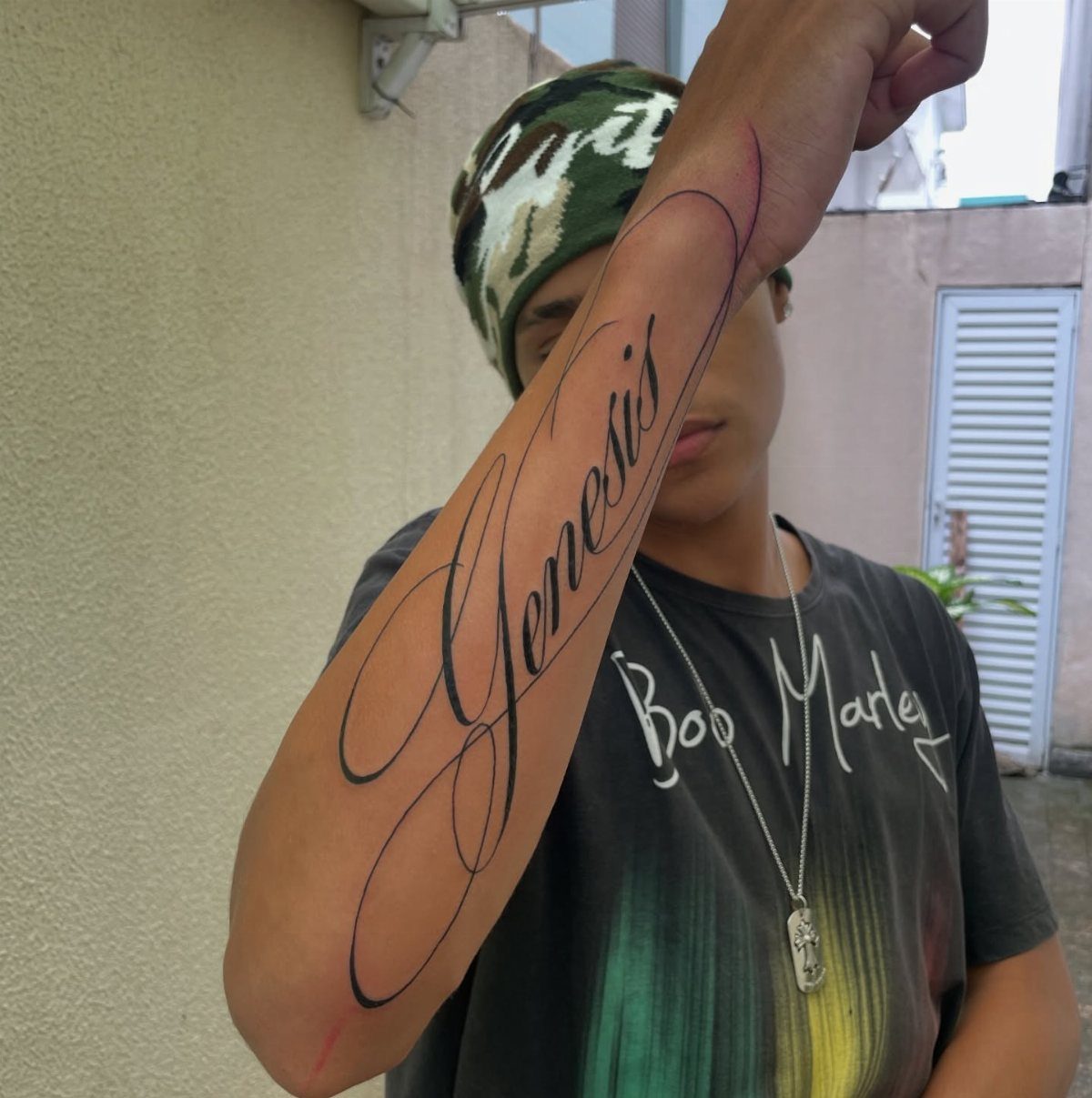 Cursive tattoo of the word Genesis on a person's forearm in black ink.
