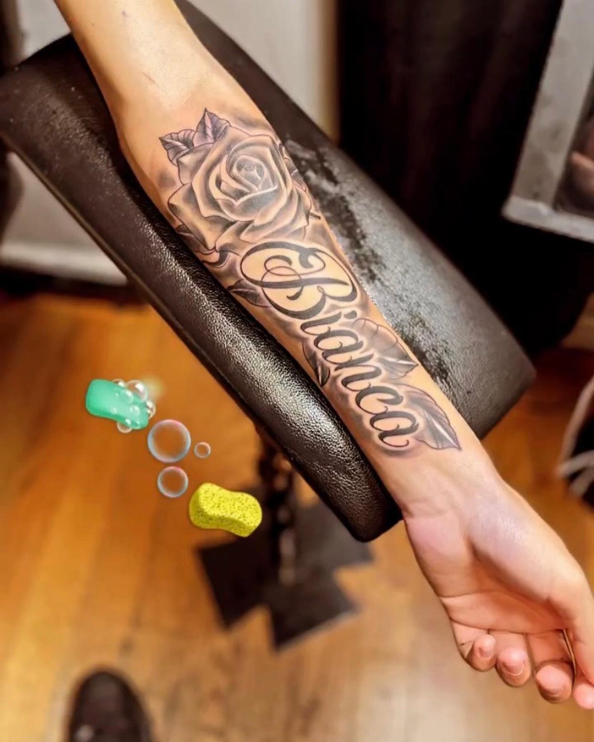 Forearm tattoo of a rose and the name Bianca in cursive script.