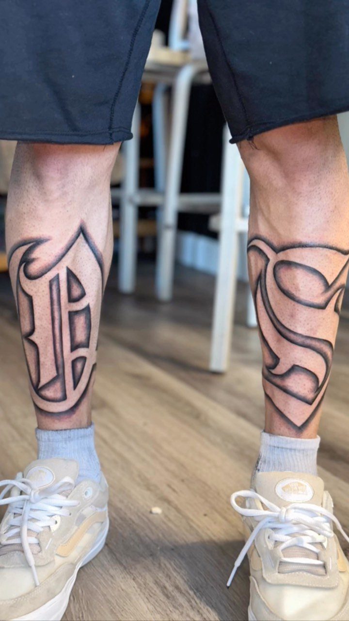 Gothic Old English style letter tattoos on a person's lower legs and ankles.