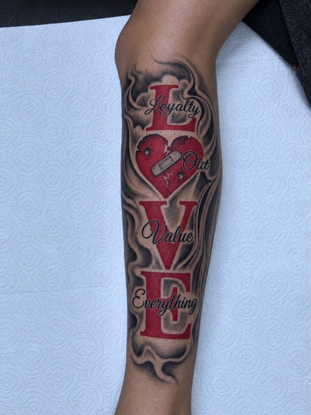 Red 3D LOVE tattoo on a forearm with a heart and grey smoke.