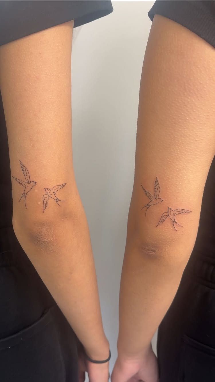 Matching tattoos of two small birds in flight on two inner elbows.
