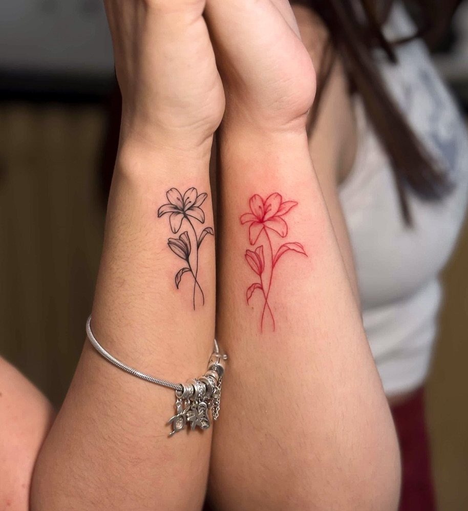 Two wrists with matching flower tattoos, one in black and one in red ink.