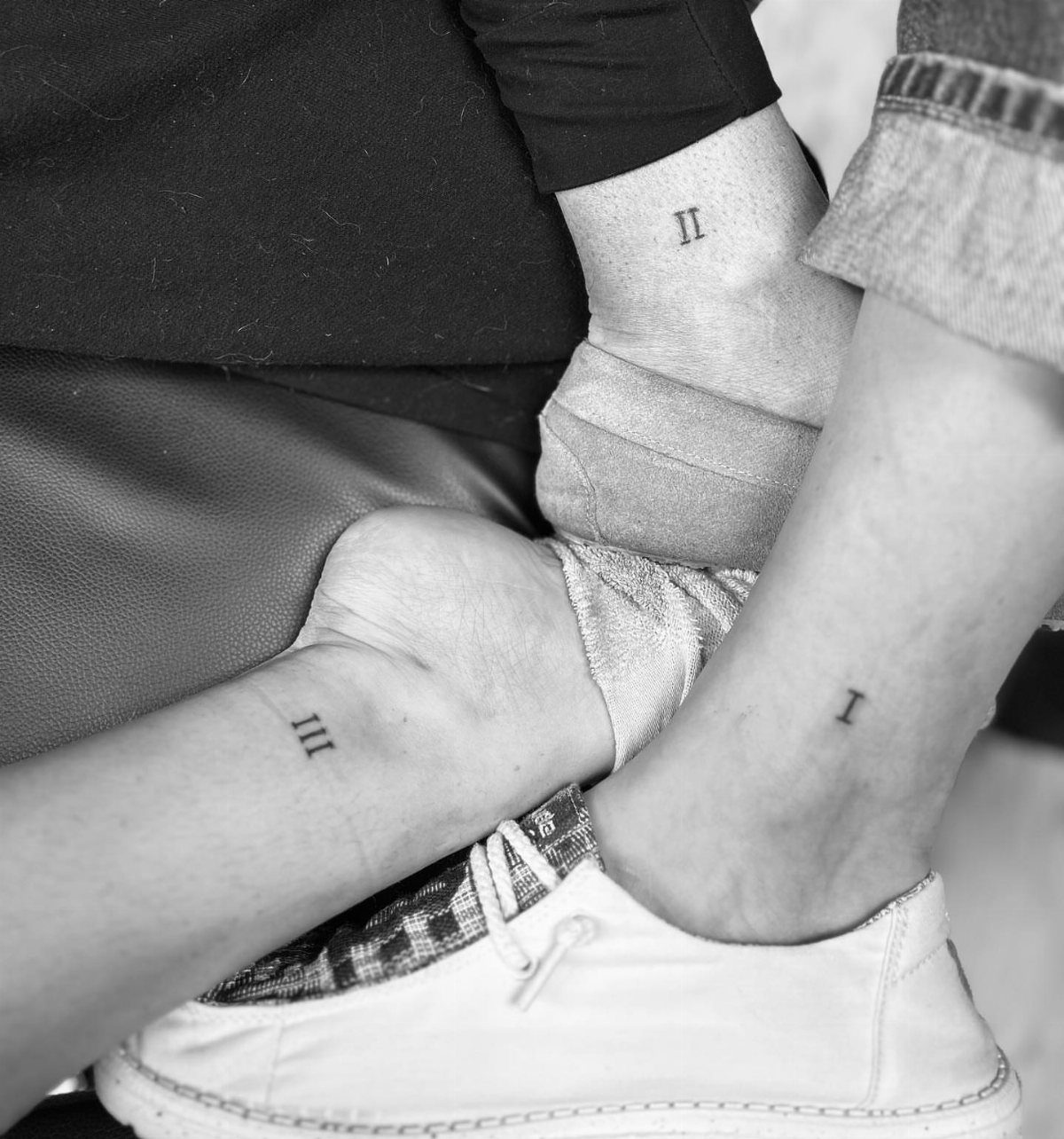 Three wrists showing matching Roman numeral tattoos for first, second, and third birth order.