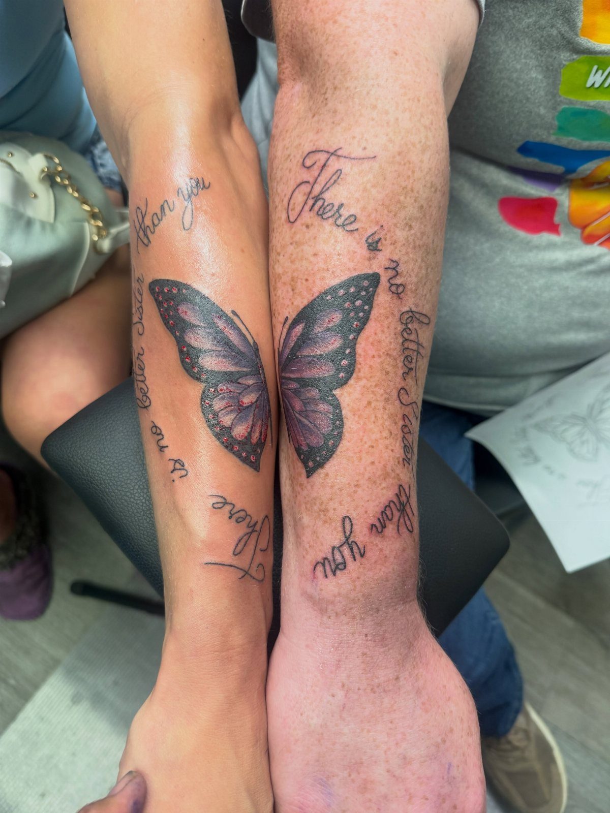 Two forearms with matching half-butterfly tattoos that connect to form one butterfly.