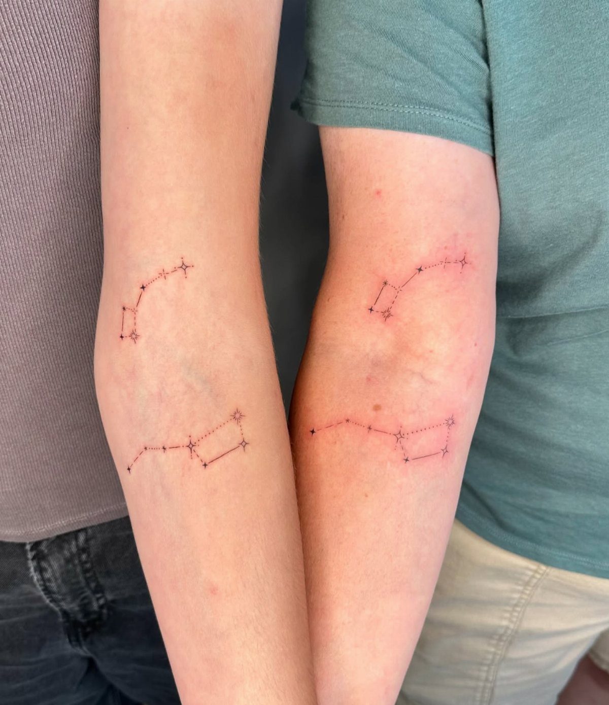 Two forearms with matching red constellation tattoos consisting of dots and lines.