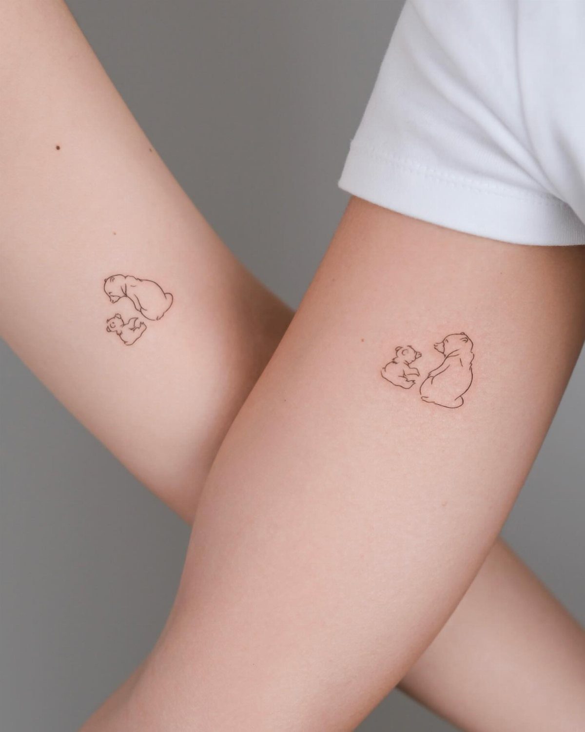 Two matching bear and cub line-art tattoos on the inner forearms of two people.