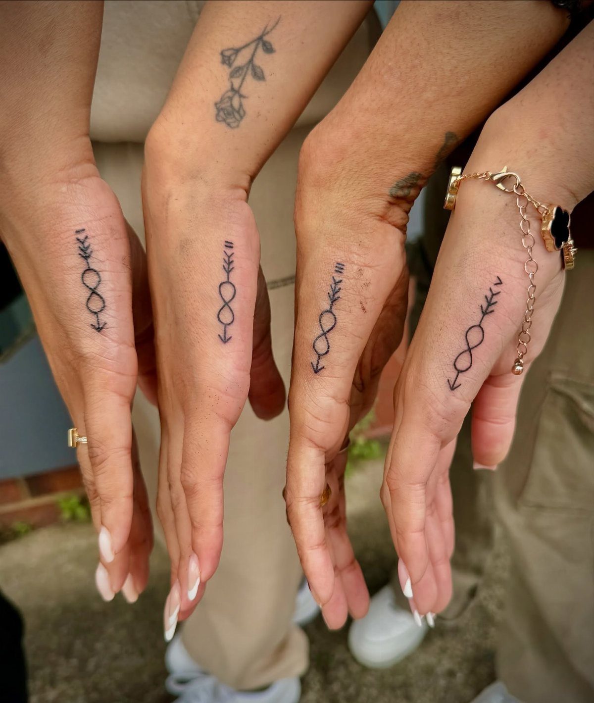 Matching infinity symbol arrow tattoos on the index fingers of four women's hands.