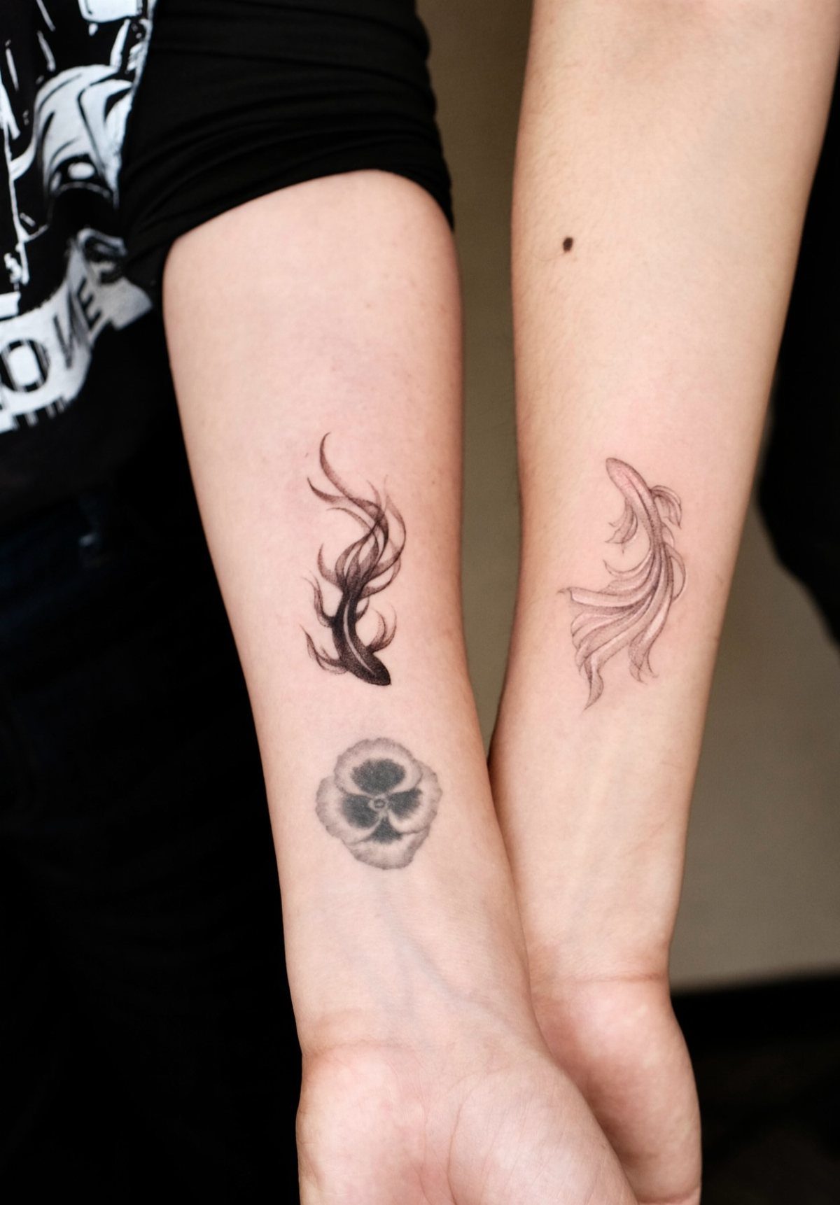 Two forearms with matching koi fish tattoos swimming toward each other in black ink.