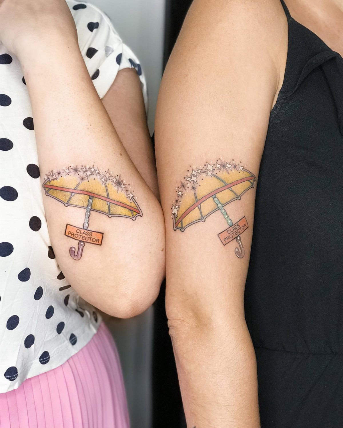Matching yellow umbrella tattoos on the upper arms of two people.