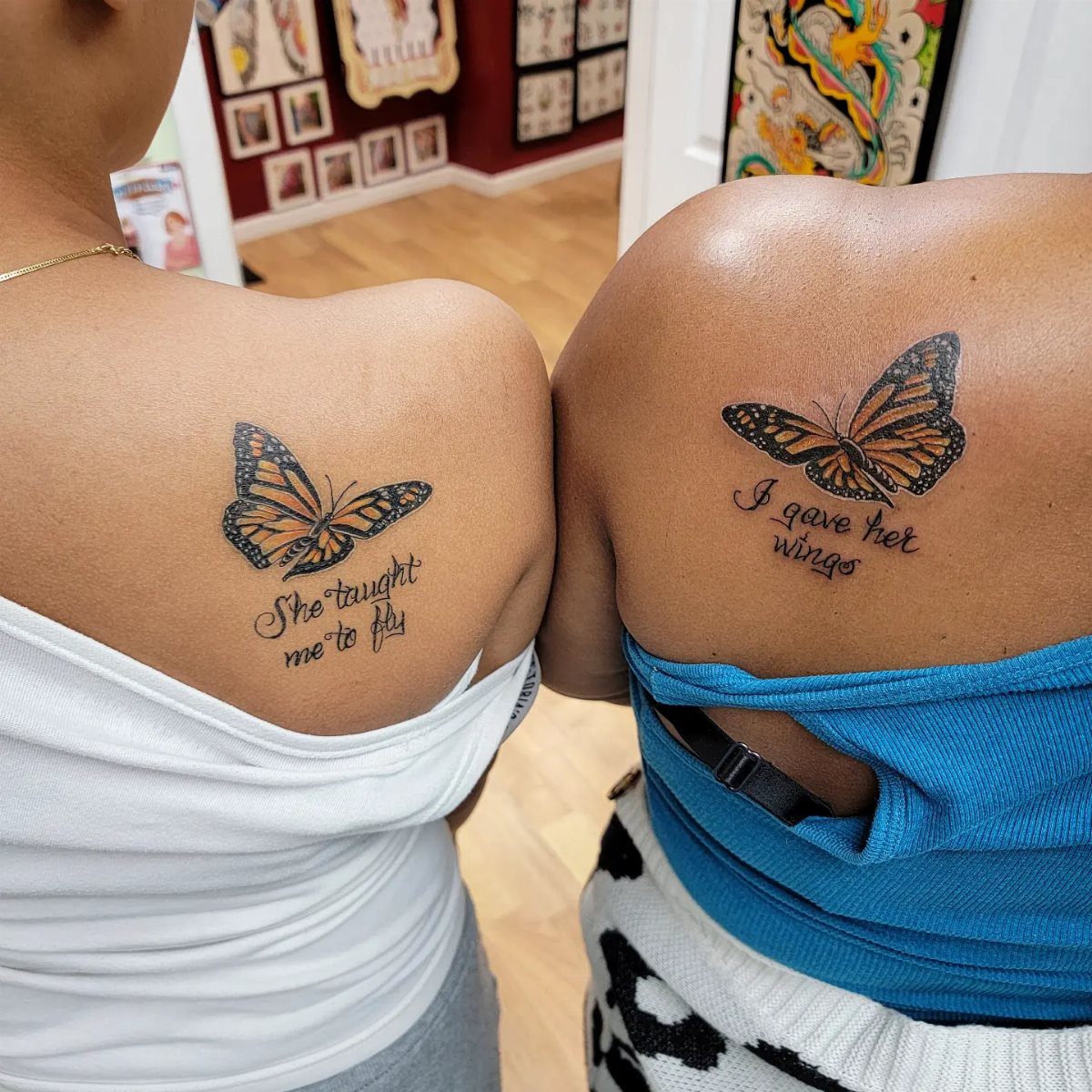 Two matching butterfly tattoos on upper backs with complementary cursive quotes.