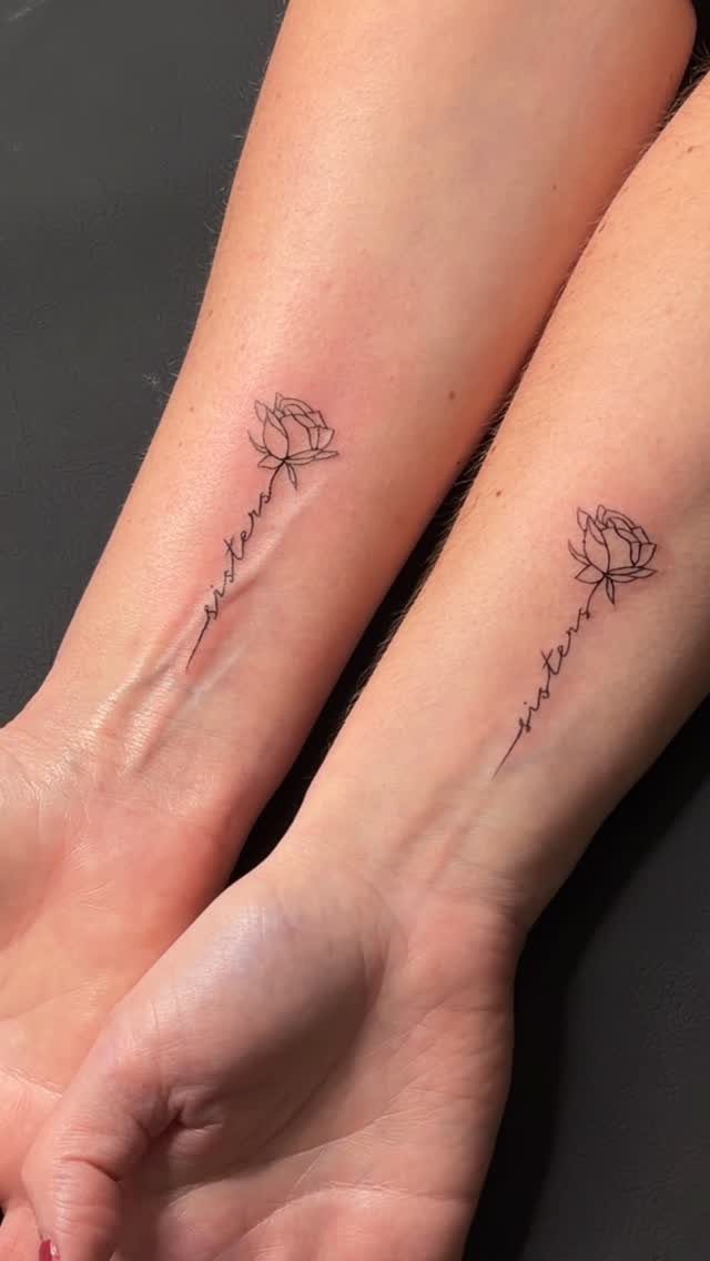 Two forearms with matching black ink rose tattoos that spell out sisters.