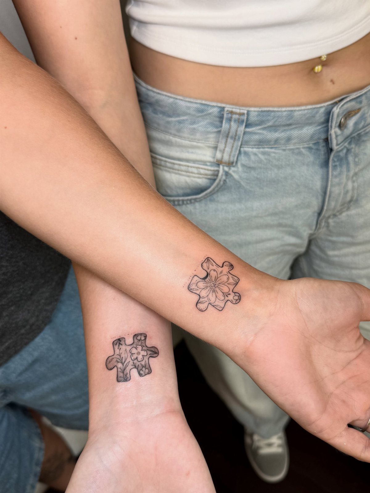 Two inner wrists with matching puzzle piece tattoos featuring floral designs inside.