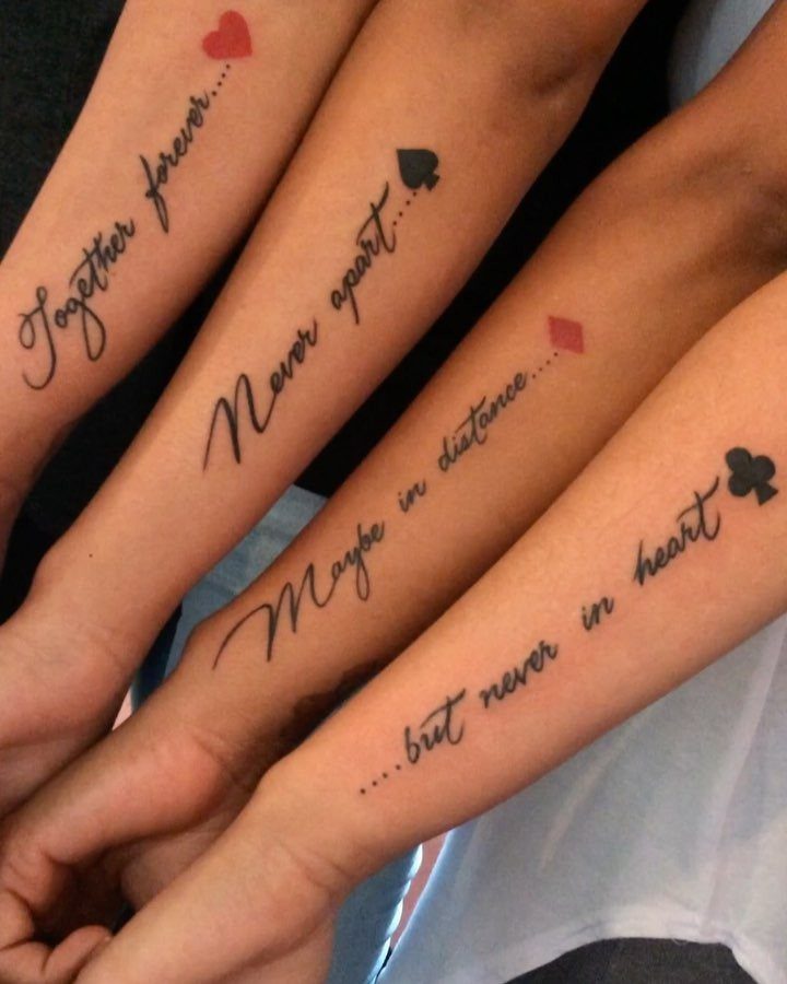 Four forearms with matching script tattoos and card suit symbols forming a sentence.