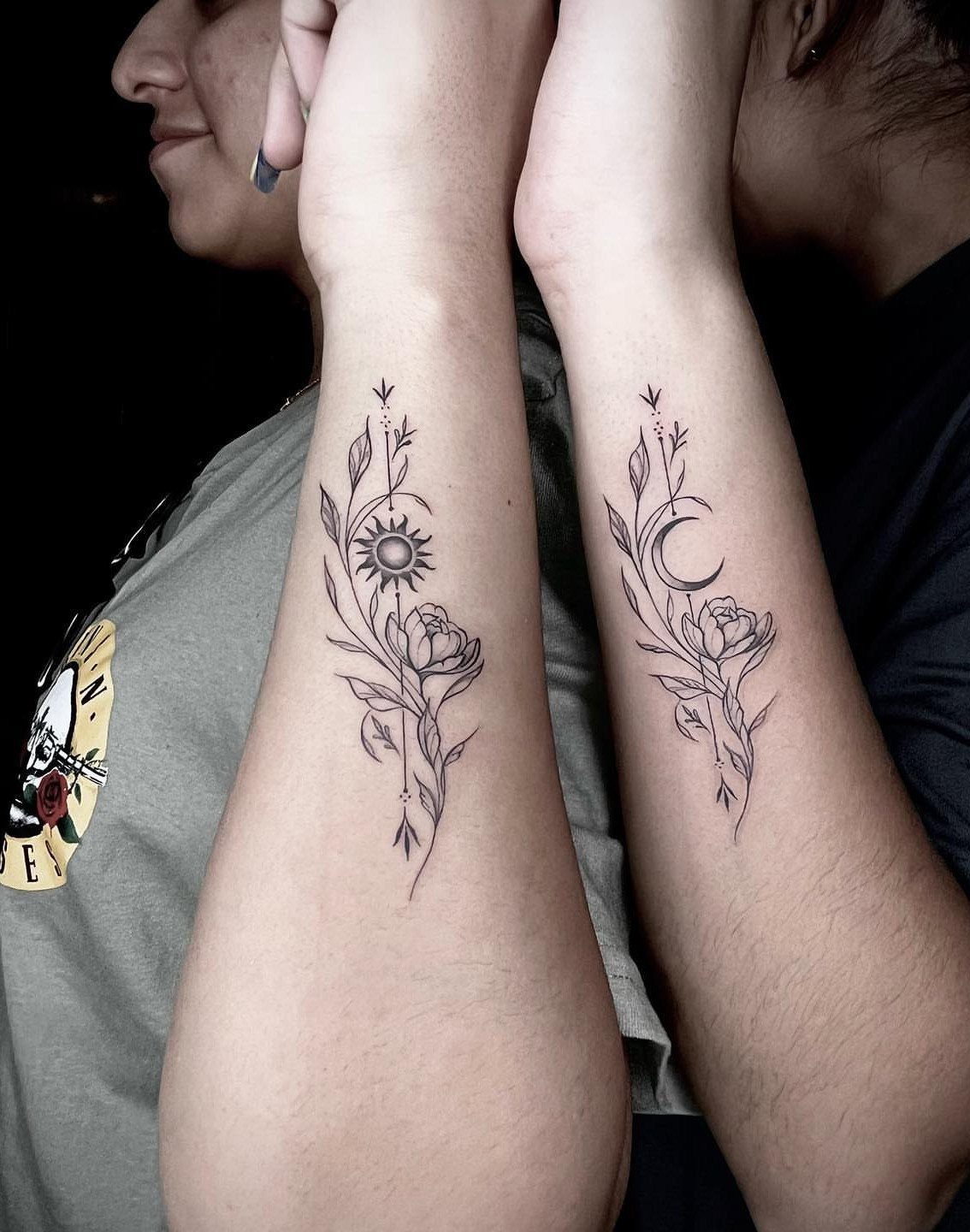 Matching sun and moon tattoos with flowers on two people's forearms.