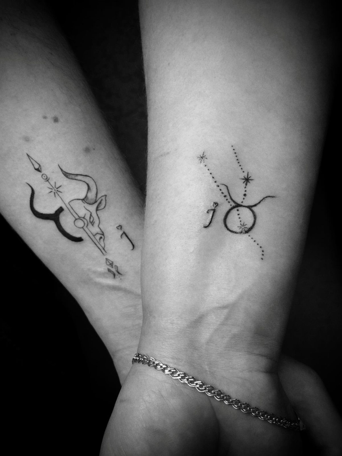 Two wrists with matching zodiac tattoos, one showing a bull and one a symbol.