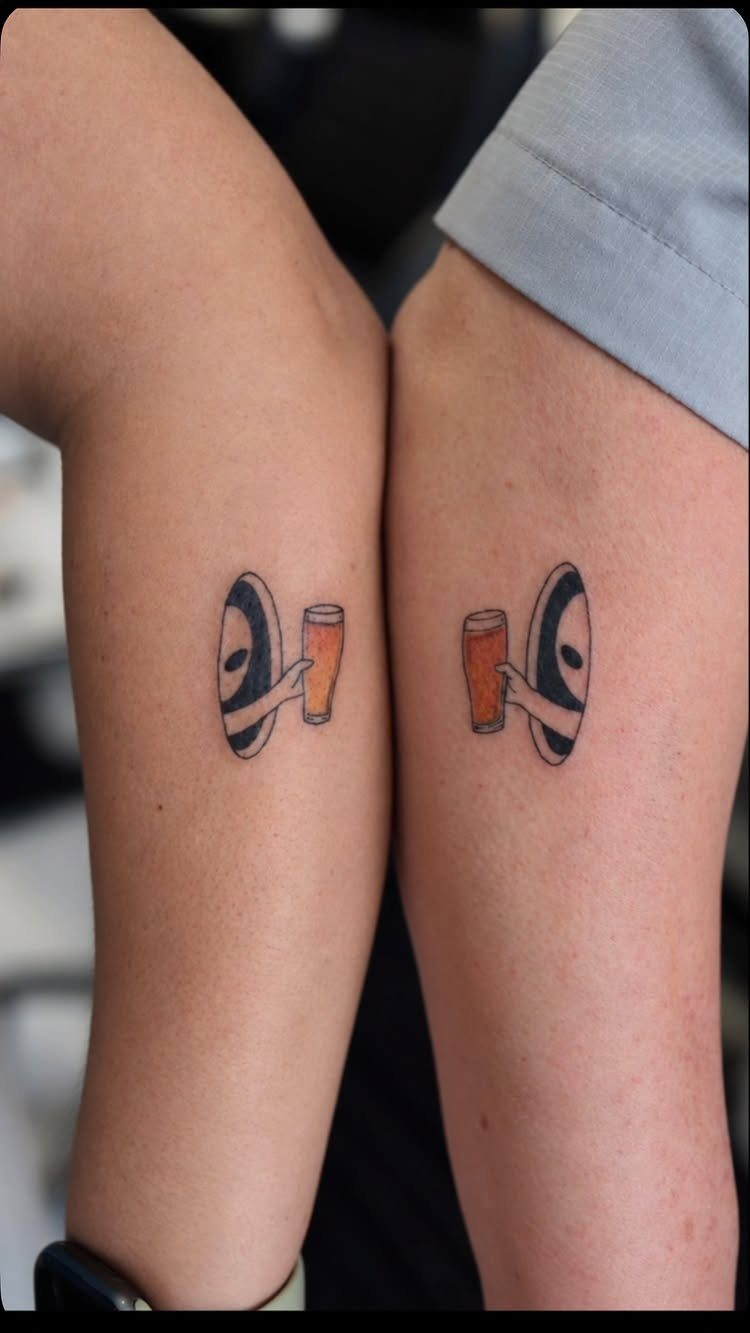 Matching tattoos of figures holding beer glasses on two people's legs.
