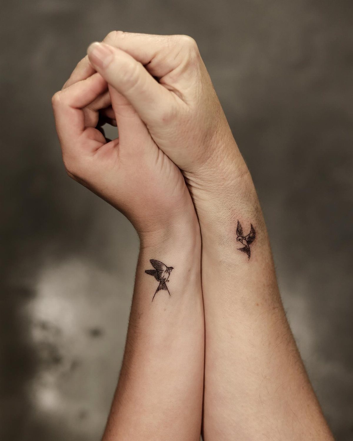 Two inner wrists with matching small black bird tattoos in flight.