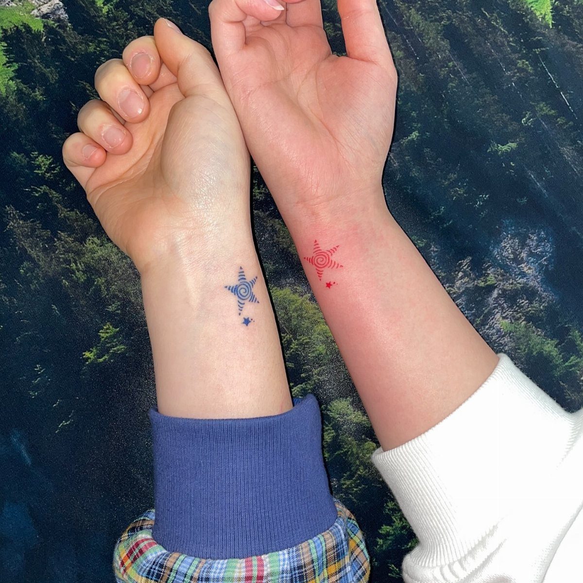 Two wrists with matching small star tattoos in blue and red colors.