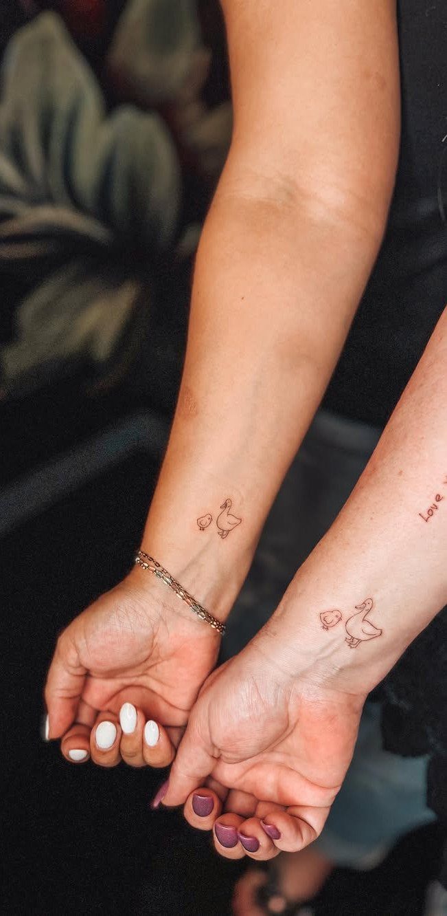Two wrists with matching small duck tattoos and colorful nail polish.