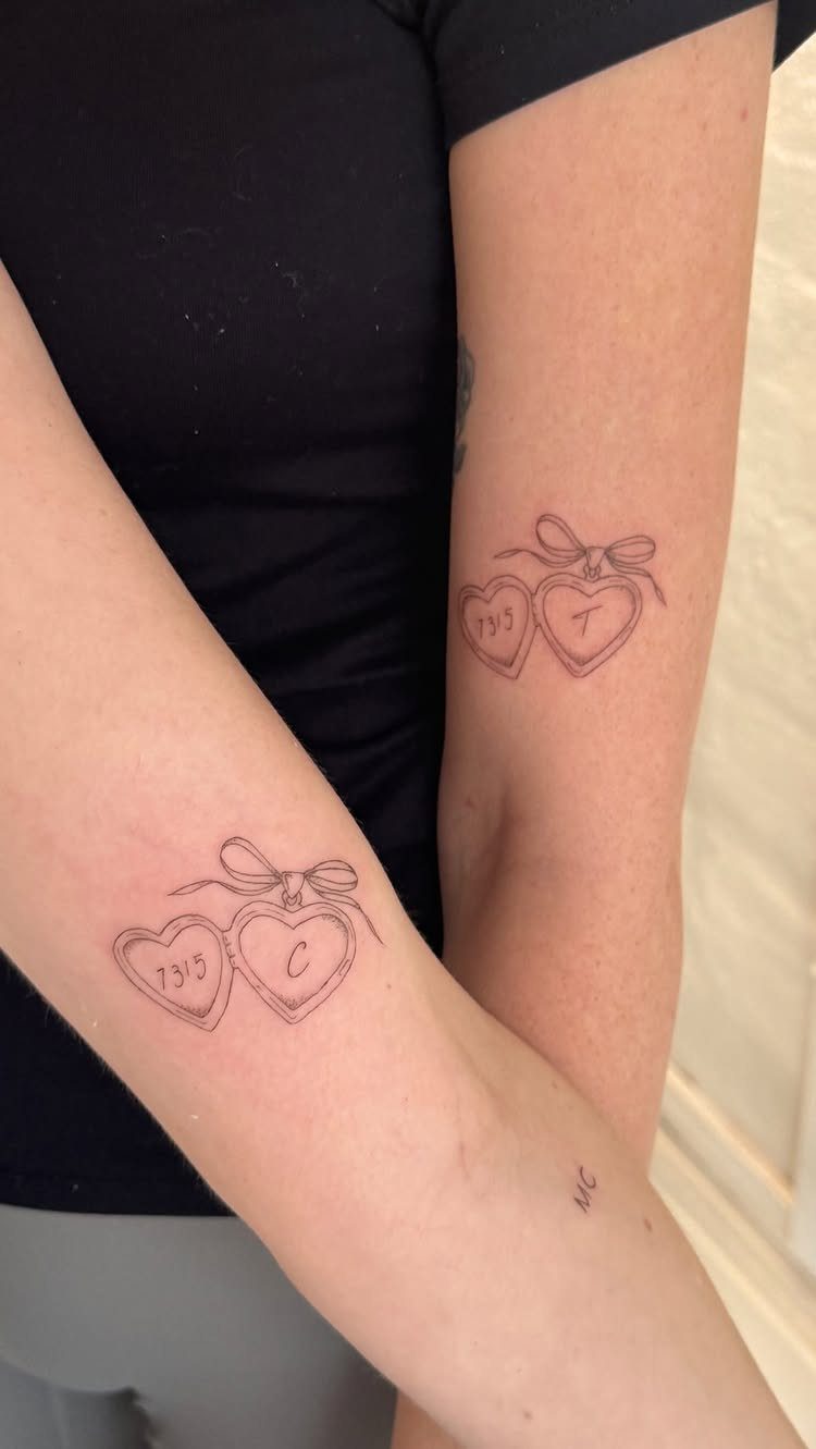 Matching heart tattoos with initials and the year 1995 on two people's arms.