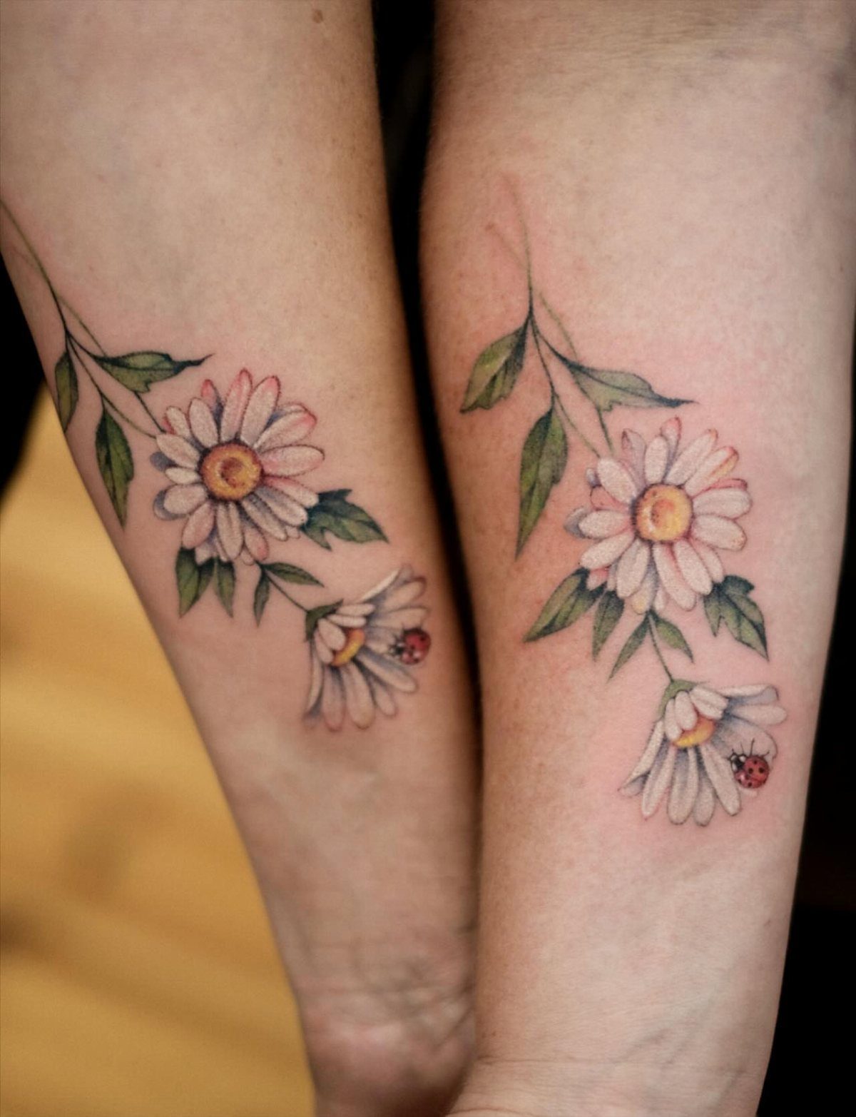 Matching daisy tattoos with ladybugs on two people's lower legs side by side