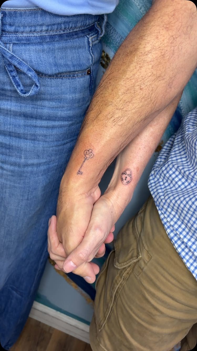 Two people holding hands with matching lock and key tattoos on their wrists.