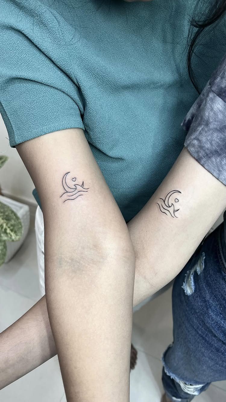 Matching tattoos of a crescent moon and ocean waves on two people's arms.