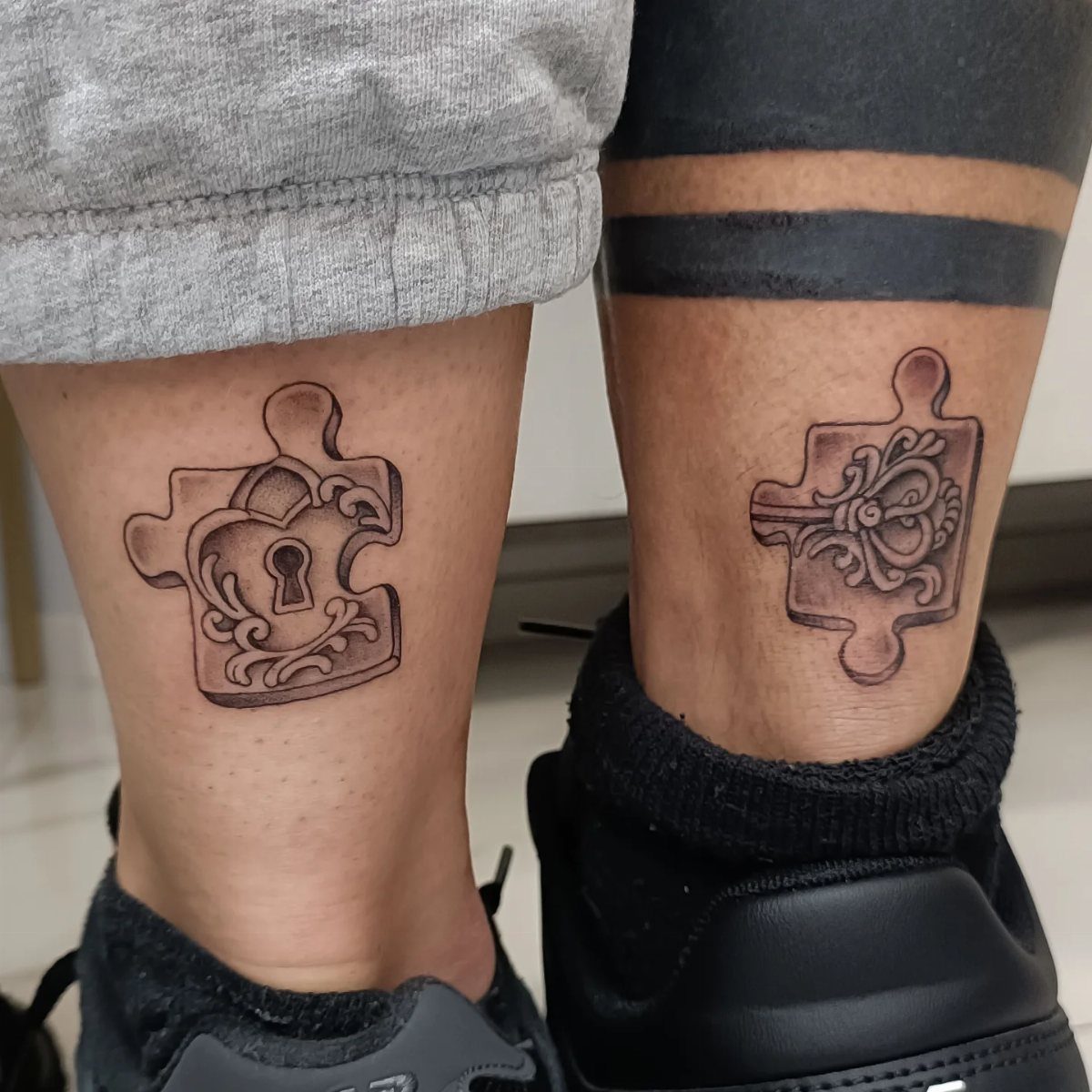 Matching puzzle piece tattoos on two ankles, one with a keyhole and one with a key.