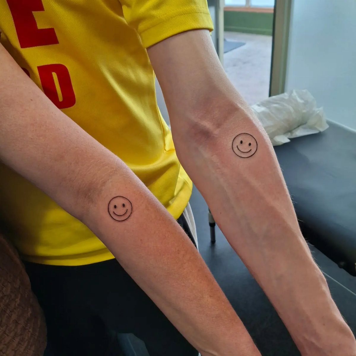 Two forearms with matching small black smiley face tattoos side by side