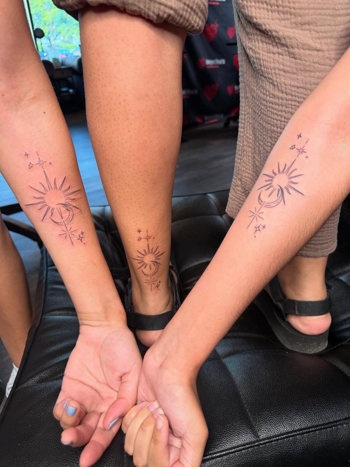 Matching sun and moon tattoos on the forearms and ankle of three people.