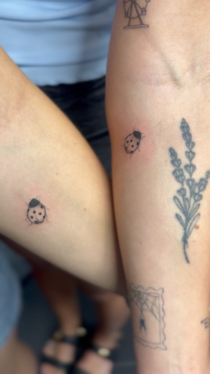 Two matching tiny ladybug tattoos on the arms of two different people.