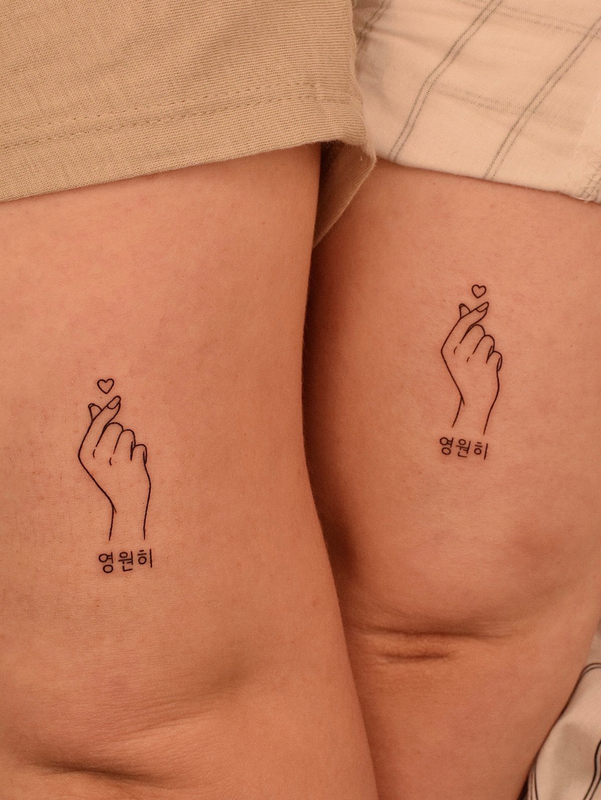 Matching finger heart tattoos with Korean text on two people's thighs.
