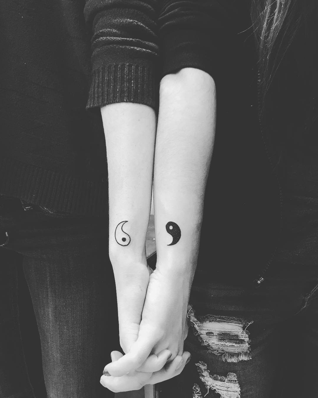Two forearms side-by-side featuring matching yin and yang symbol tattoos on the wrists.