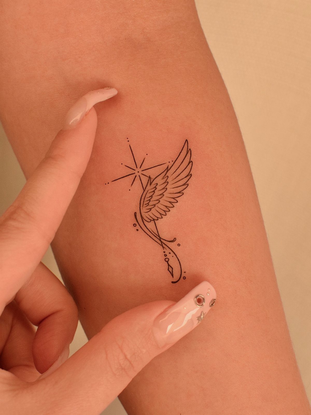 Small black ink tattoo of an angel wing and star on skin.