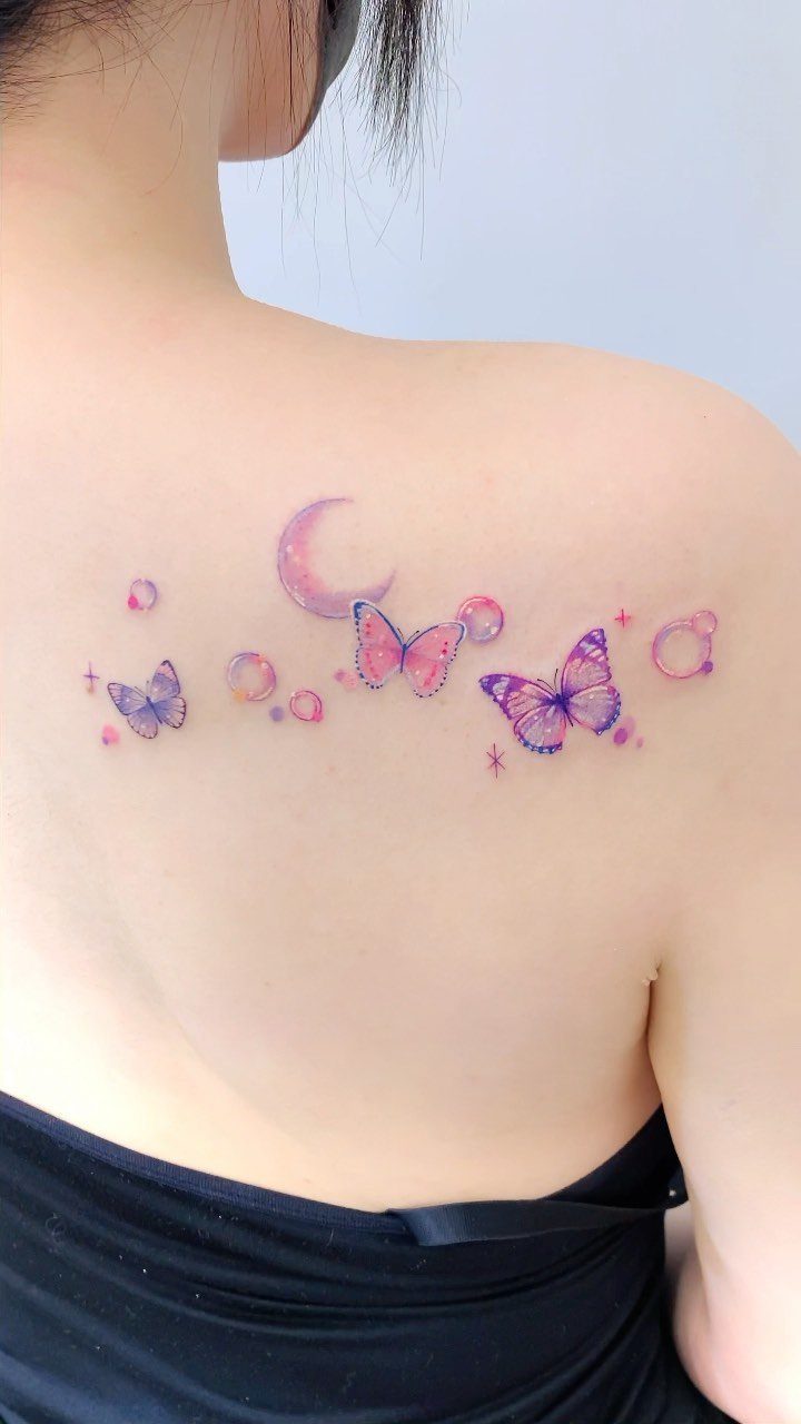 Three colorful butterfly tattoos with a crescent moon on a person's upper back.