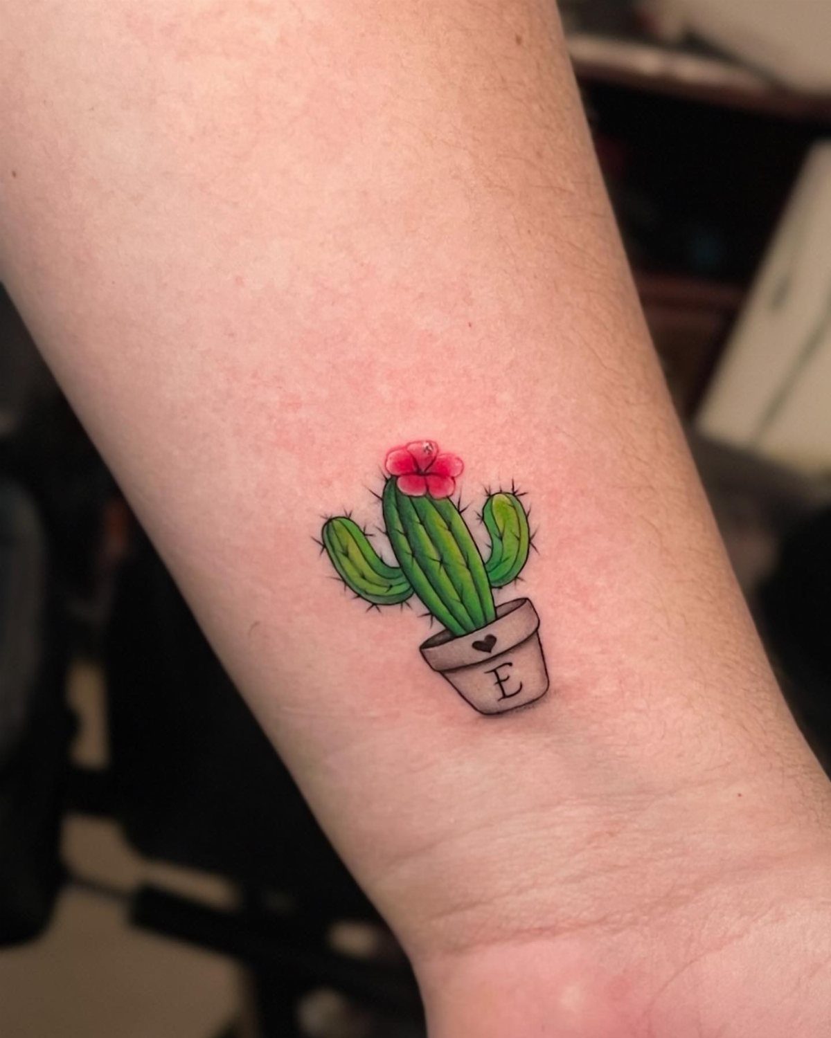 Small cactus tattoo with a pink flower in a pot on a wrist