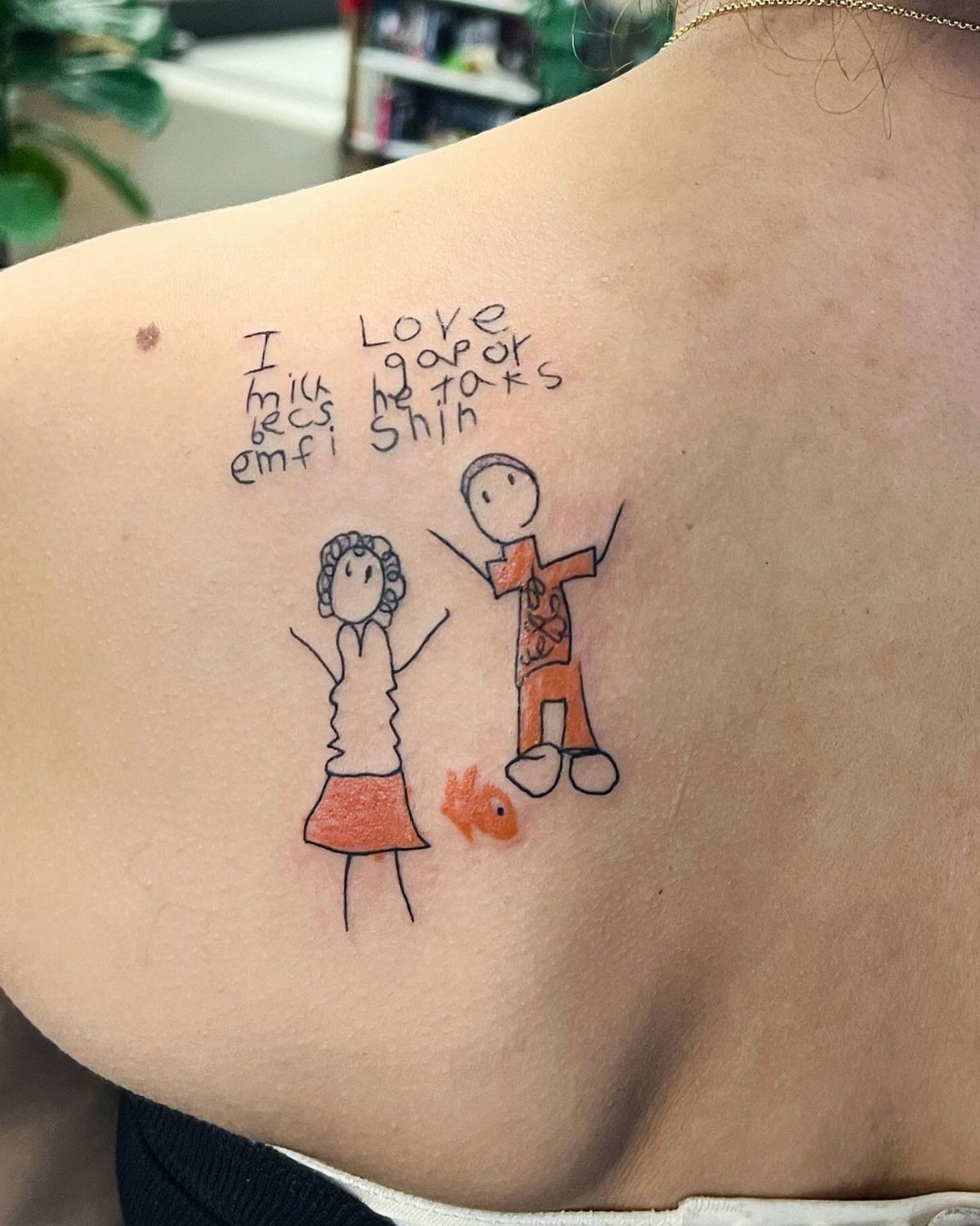 Child's drawing tattoo of two stick figures and handwritten text on a shoulder.