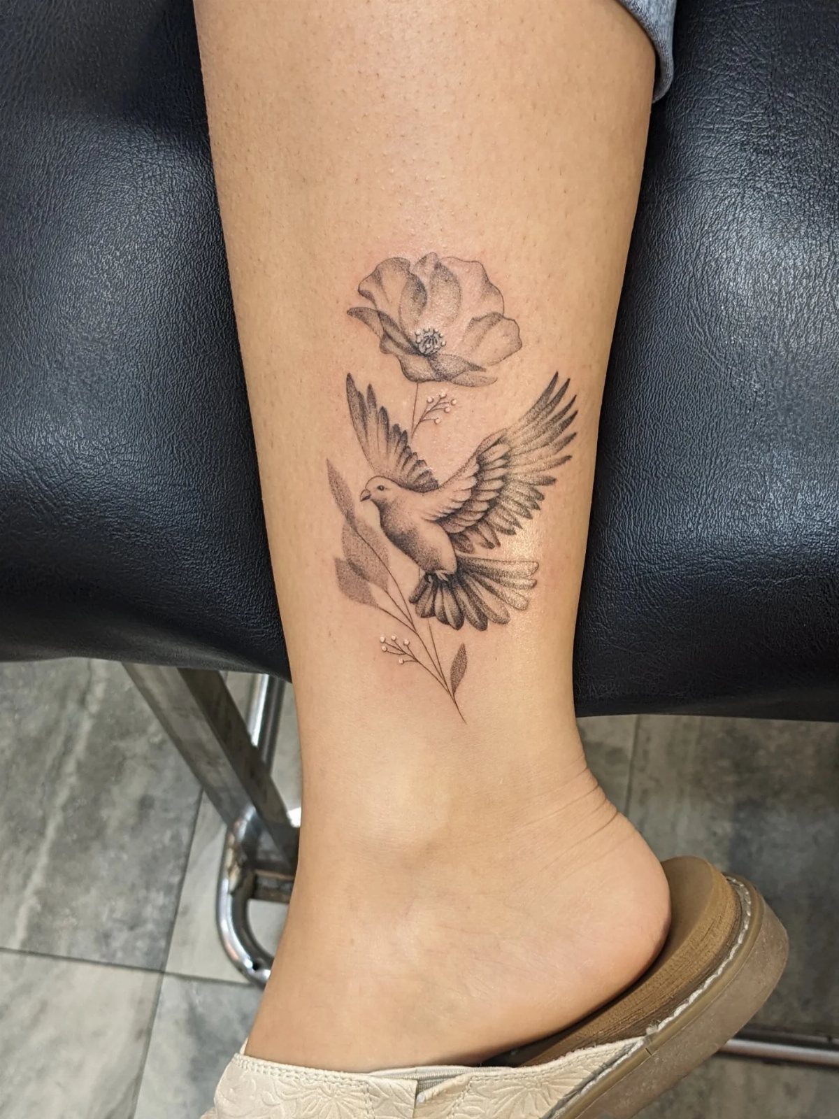 Dove tattoo with a flower and leaves on a person's ankle