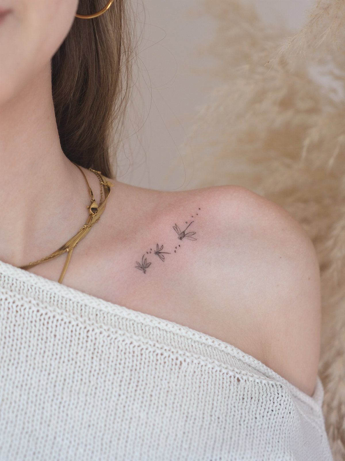 Three tiny minimalist dragonfly tattoos in black ink on a person's shoulder