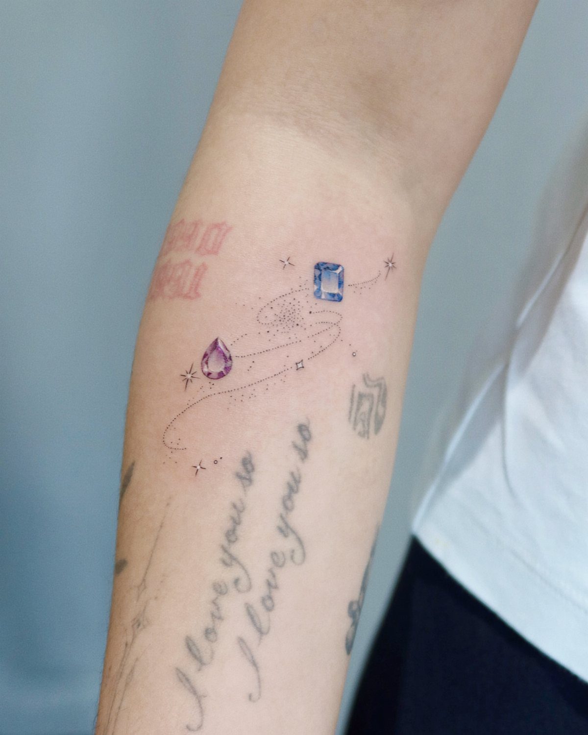 Small blue and purple gemstone tattoos with stars on a person's forearm.